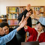 Group of happy students high-fiving in a library setting, celebrating success.